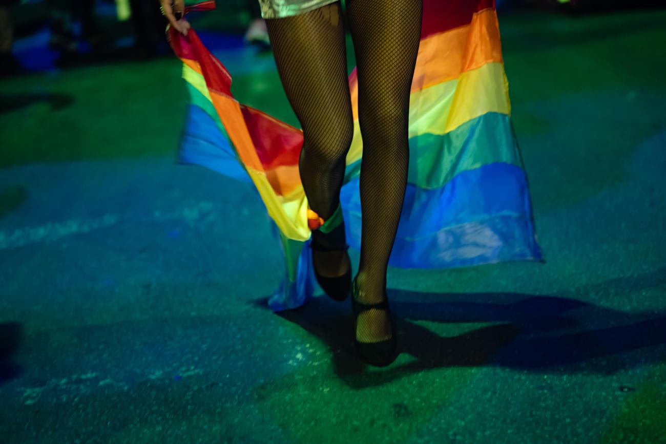 Foto de la marcha de la diversidad, muestra unas piernas y una bandera de la diversidad. 